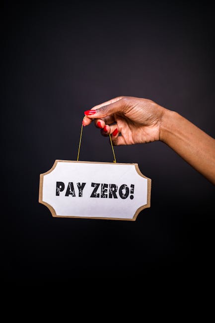 A close-up of a person's hand with red nail polish holding a small, ornate sign with a gold border and a string, displaying the text 'PAY ZERO!' in bold, black letters. The background is dark and plain, with no other objects or context visible related to house removals or moving services. This image emphasizes the concept of cost-free or zero charges, relevant to relocation or moving quotes, and may be used on a website like removalcompanieselephantandcastle.co.uk to highlight promotional offers or payment terms in the removals service category.